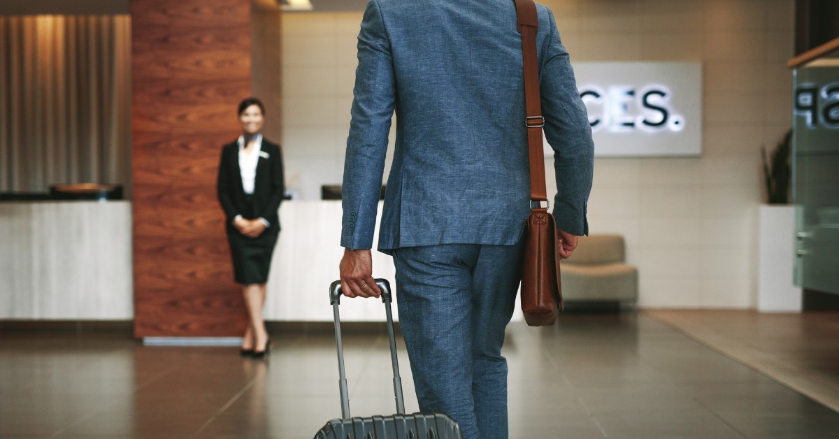 A man in a suit walking through a hotel lobby with a suitcase