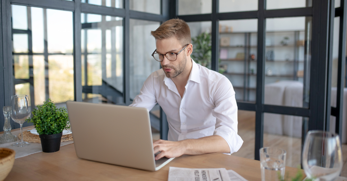 A man in a suit wearing glasses and typing on a laptop