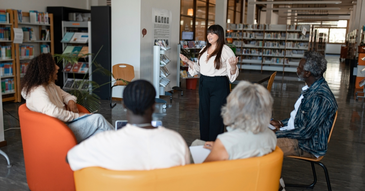 A woman standing in a library speaking to a group of people