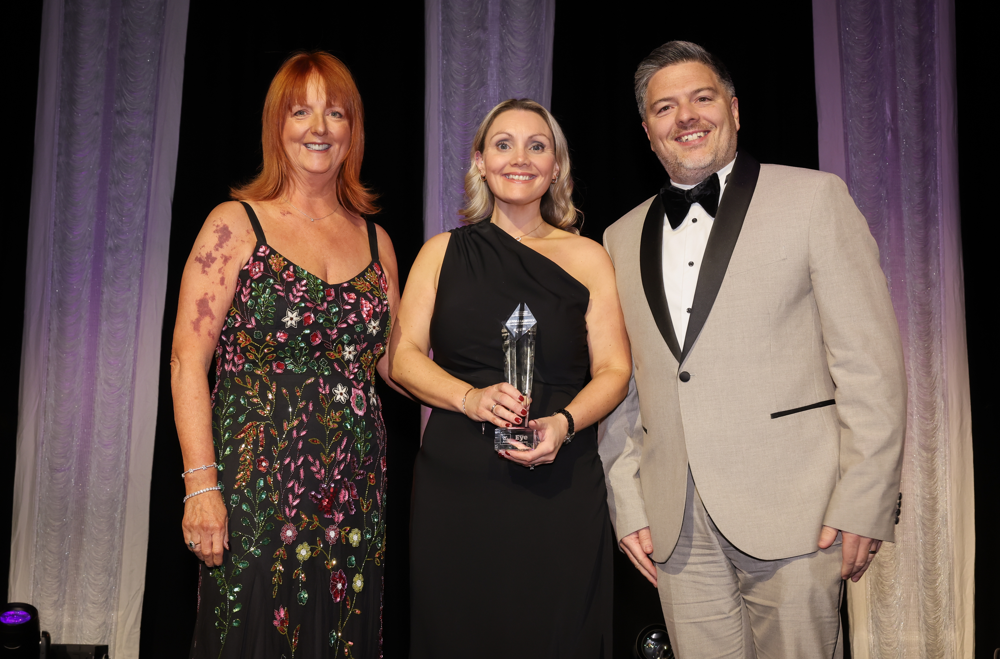 3 people smiling holding an award